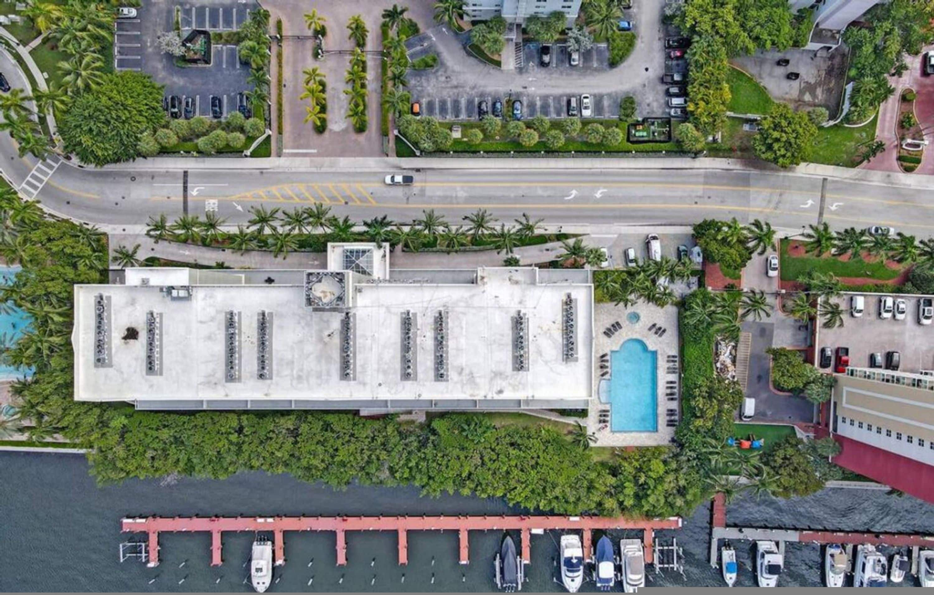 Vista aérea de un hotel con un amplio estacionamiento, piscina y un puerto deportivo con barcos.