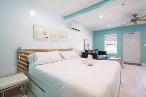 A bedroom with a large bed, a bench, a small table, a ceiling fan, and artwork on the wall. - Casa Del Mar Deluxe Studio 2 (Hollywood)