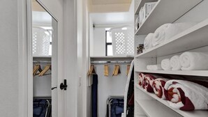 Habitación de hotel con un armario que contiene toallas dobladas con cuidado, una silla azul y un carrito metálico.
