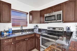 A kitchen with wooden cabinets, a stainless steel microwave, an oven, a sink, and a window with blinds. - New Waves on Walnut 1 (Hollywood)