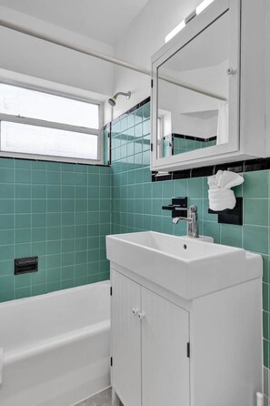 Un baño moderno con azulejos verde azulado, un lavamanos blanco y una bañera.