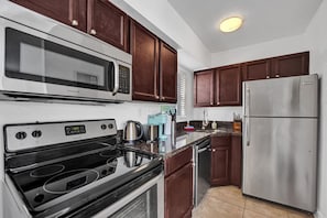 Una cocina moderna con armarios de madera oscura, electrodomésticos de acero inoxidable, incluyendo un refrigerador, microondas y estufa, además de un horno empotrado.