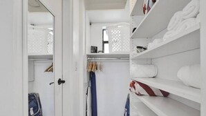A walk-in closet with shelves for folded towels, a rack for hanging clothes, and a door leading to another room. - Waves On Walnut 2-beach Access (Hollywood)