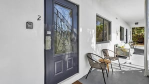 A modern building entrance with a dark door, numbered 2, and a small outdoor seating area with two chairs and a table. - Waves On Walnut 2-beach Access (Hollywood)