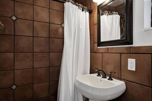 A bathroom with a white sink, brown tiled walls, and a white shower curtain.