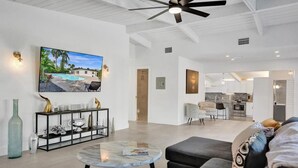 Un salón amplio con un moderno ventilador de techo, un televisor de pantalla plana grande, una zona de comedor y una cocina.