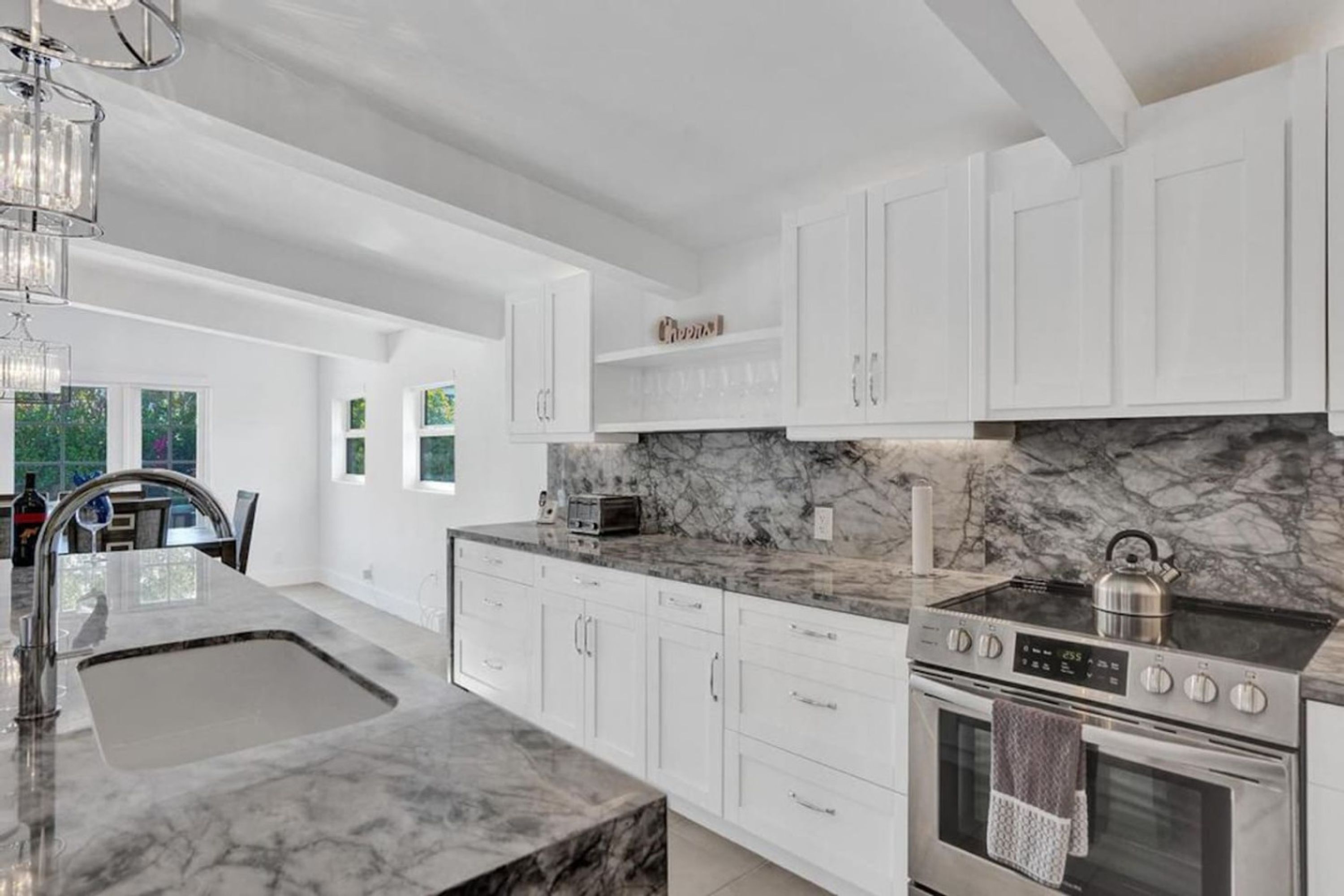 A modern kitchen with white cabinets, a marble countertop, a built-in stove, and a sink.