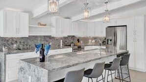 Una cocina moderna con armarios blancos, una isla de mármol, taburetes de bar e iluminación colgante.