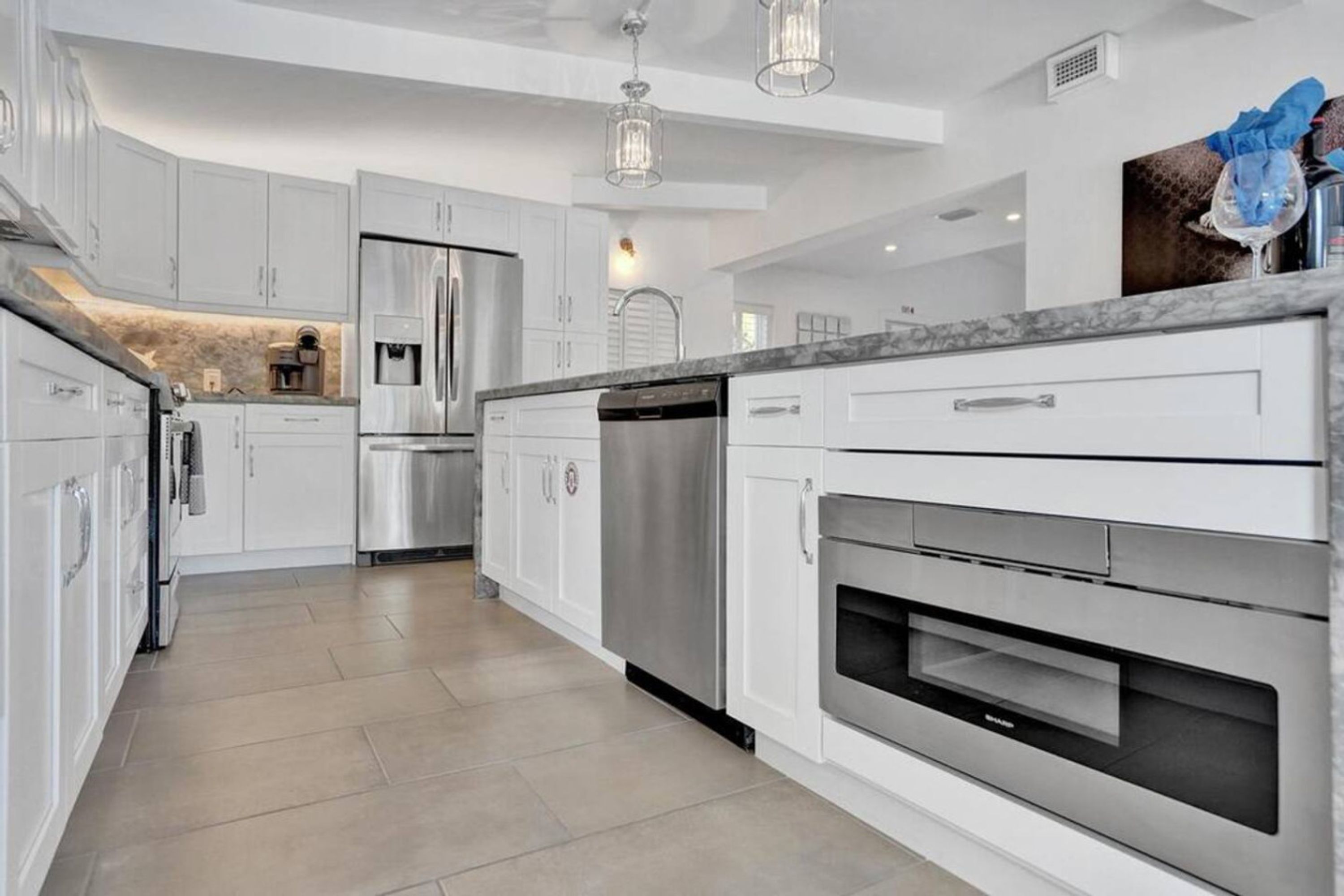 A modern kitchen with white cabinetry, stainless steel appliances, and a marble countertop.
