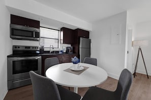 A modern kitchen with dark cabinets, stainless steel appliances, and a round dining table with four chairs.