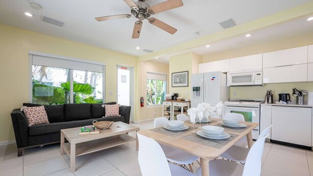 A modern living room with a sofa, coffee table, dining table with chairs, a ceiling fan, and a kitchen area with appliances. - Casa Del Mar 5 Beach Access (Hollywood)