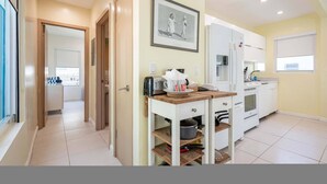 A modern kitchen with white cabinets, a wooden countertop, and a built-in oven. There is a framed picture on the wall and a window with blinds. - Casa Del Mar 5 Beach Access (Hollywood)