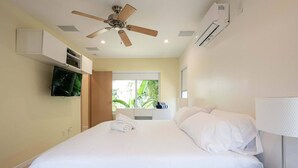 A hotel room with a bed, a ceiling fan, a TV, and a window with a view of greenery. - Casa Del Mar 5 Beach Access (Hollywood)