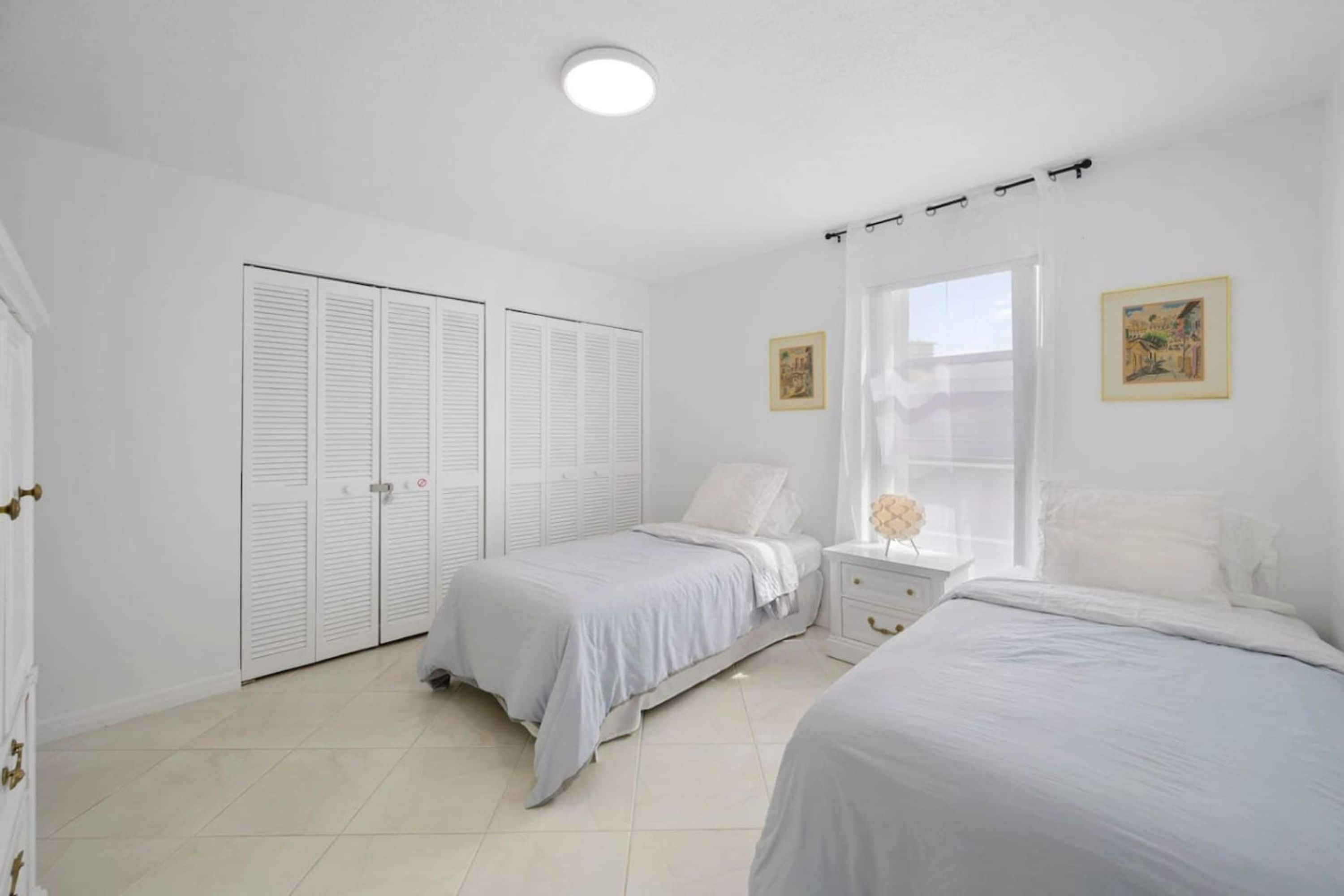 A bedroom with two beds, a window with curtains, and a white wardrobe.
