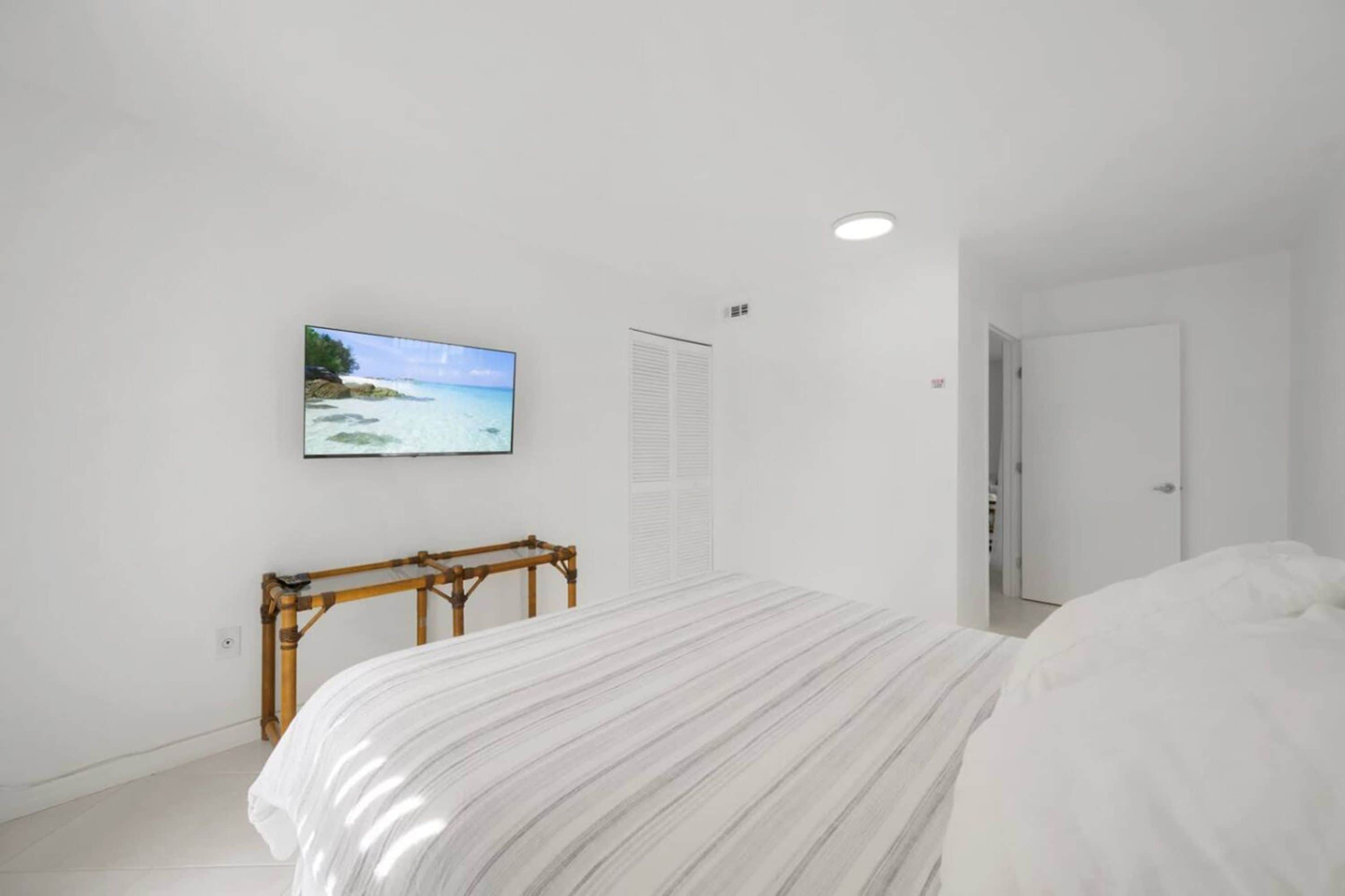 Ein Schlafzimmer mit einem Bett, einem an der Wand befestigten Fernseher, einer hölzernen Bank und einer Tür.