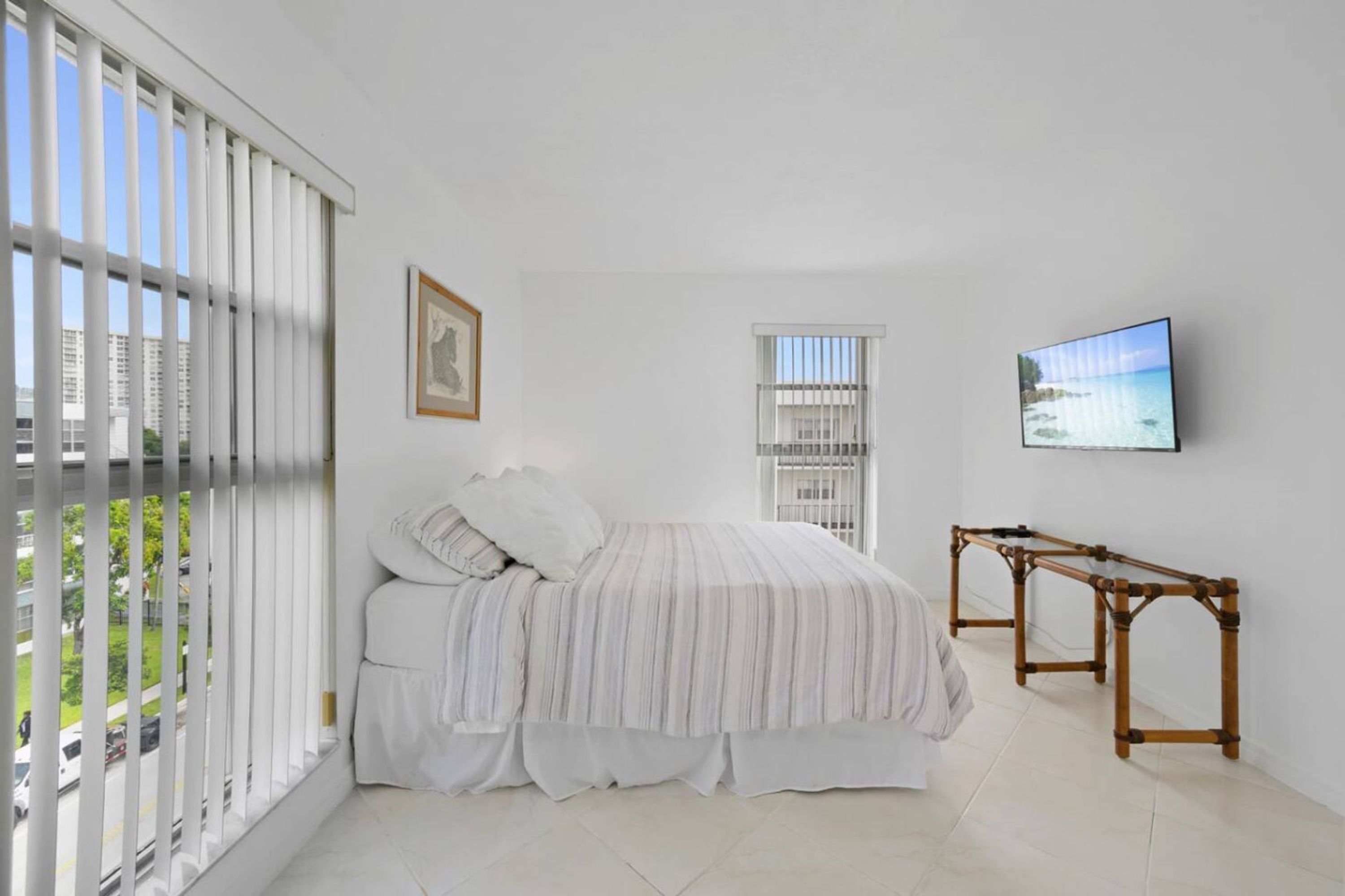 Un dormitorio con cama, televisor y ventana con persianas.