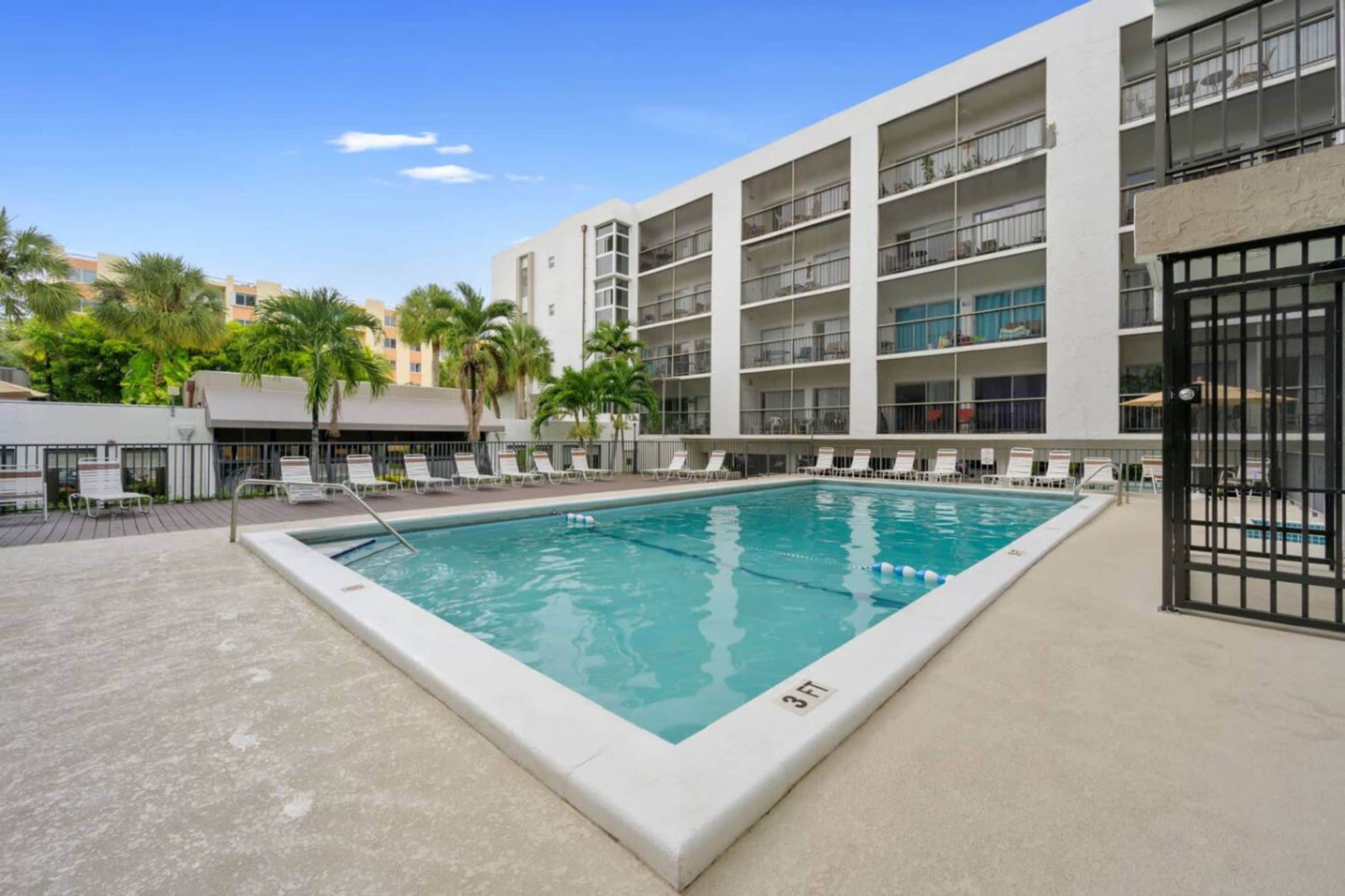 A swimming pool with lounge chairs and a building with balconies in the background.