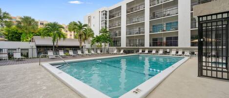 A swimming pool with lounge chairs and a building with balconies in the background.
