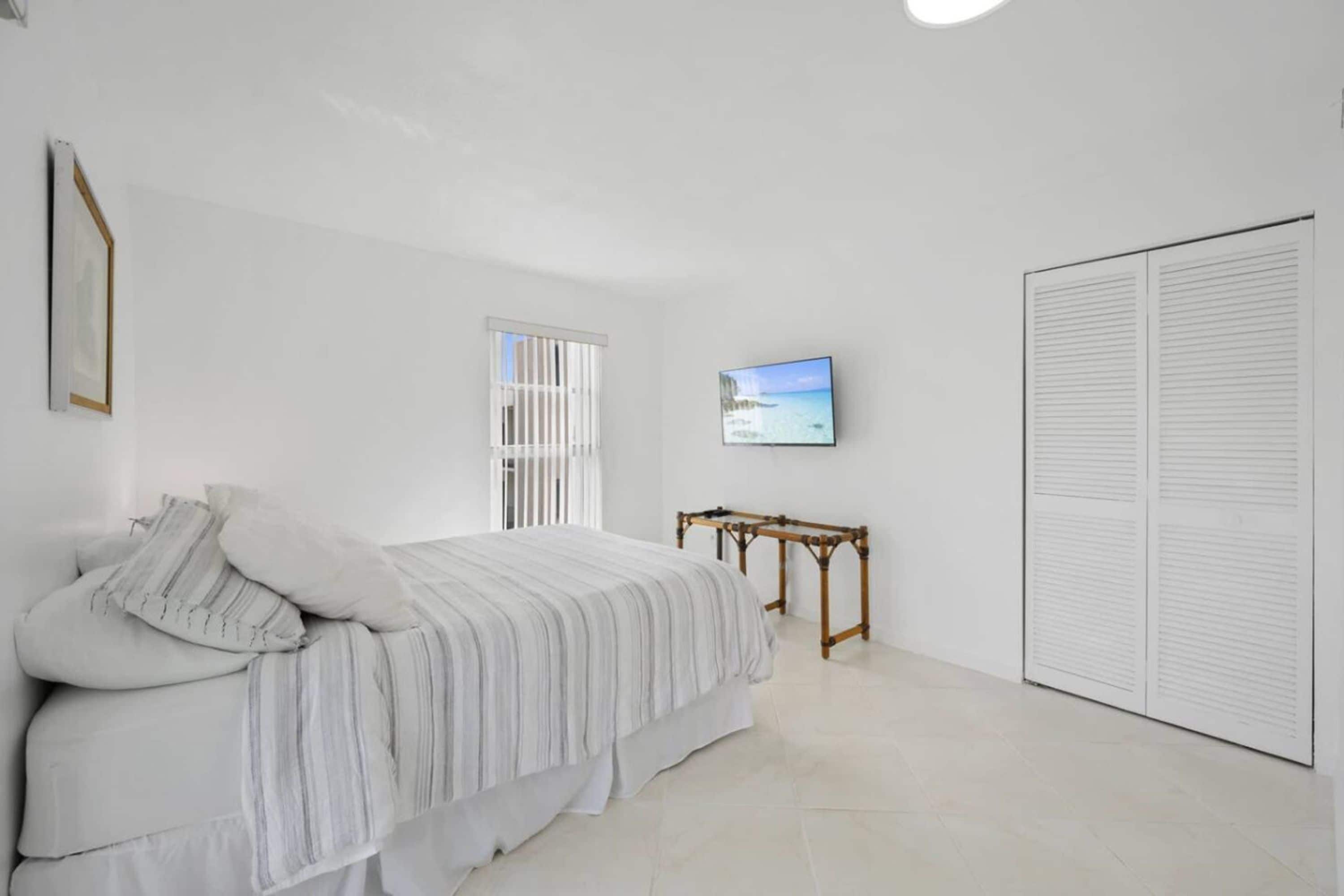 Quarto com cama, televisão na parede, janela e armário.