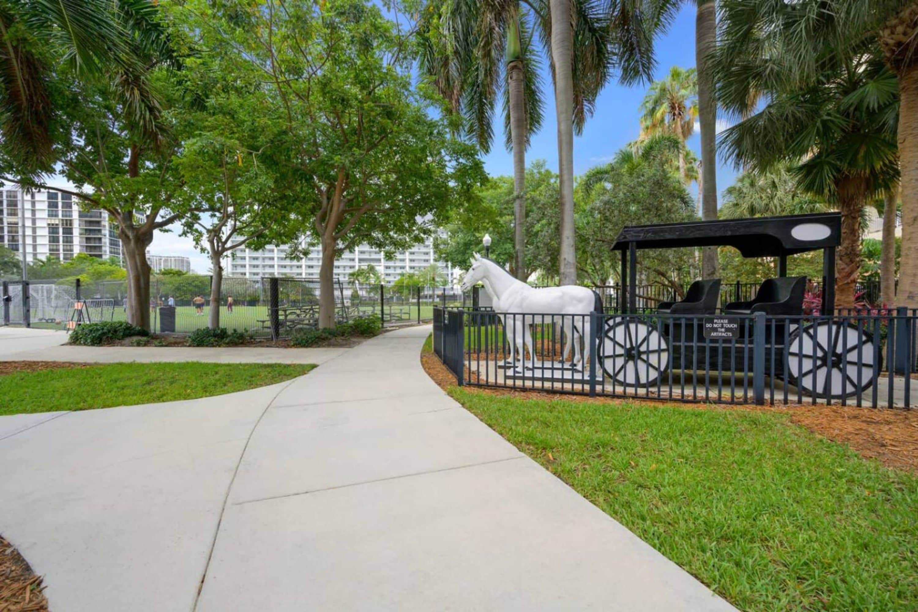 A pathway lined with palm trees and a white horse statue.