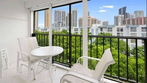 A balcony with white chairs and a table, offering a city view through large windows. - le Cartier Sunny Isles Ocean Paradise (Sunny Isles Beach)