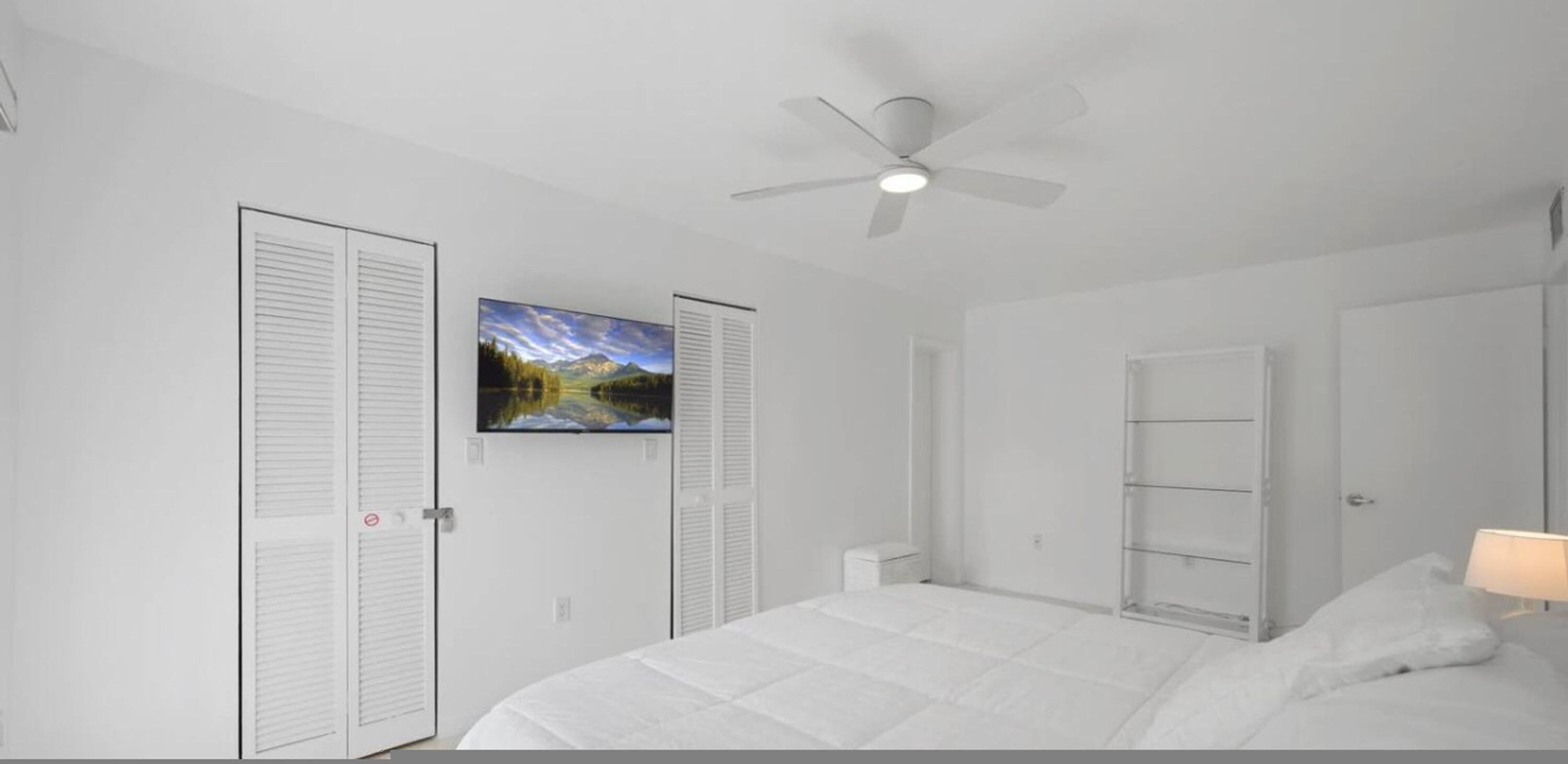 A bedroom with a bed, a ceiling fan, a painting, and a wardrobe.
