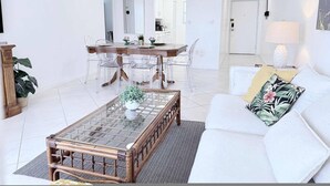 A spacious living room with a white sofa, a glass-top coffee table, and a dining area with a wooden table and clear chairs. - le Cartier Sunny Isles Ocean Paradise (Sunny Isles Beach)