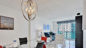 A modern dining area with a glass table, red and black chairs, a chandelier, and a city view through large windows. - New New Beach View (Hollywood)