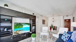 A modern living room with a flat-screen TV, a glass coffee table, and a sofa with patterned cushions. - New New Beach View (Hollywood)