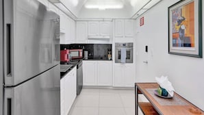 A modern kitchen with white cabinets, stainless steel appliances, and a dining area with a table and chairs. - New New Beach View (Hollywood)