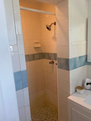 Eine kleine, geflieste Dusche mit einer Handbrause, einer Seifenschale und einem Handtuchhalter an der Wand.