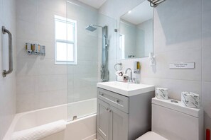 A modern bathroom with a glass shower enclosure, a vanity with a mirror, and a sign instructing to flush only toilet paper.