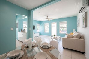 A modern living room with a sofa and a dining area with a glass table and chairs. - Casa Del Mar 4 1 1 Beach Access (Hollywood)
