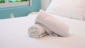 A neatly made bed with a rolled white towel, a window with blinds, and a framed picture on the wall. - Casa Del Mar 4 1 1 Beach Access (Hollywood)