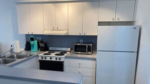 A compact kitchen with white cabinets, a stove, a microwave, and a refrigerator.