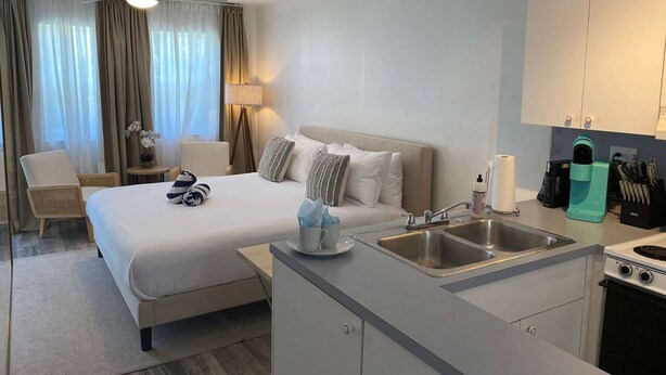 A hotel room with a bed, bedside table, lamp, chair, and kitchenette.
