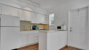 A compact kitchen with white cabinets, a microwave, and a small window.