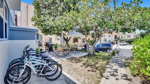 A residential area with bicycles parked against a building, a tree, and a patio with outdoor furniture.