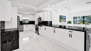 A modern kitchen with white cabinets, black countertops, and a marble island. - Hibiscus House in Fort Lauderdale (Fort Lauderdale)