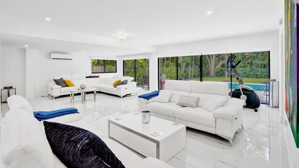 A modern living room with white furniture, large windows, and a view of greenery outside. - Hibiscus House in Fort Lauderdale (Fort Lauderdale)