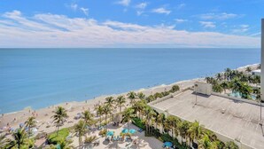 Vista de una playa con palmeras, piscina y un edificio de techo plano.