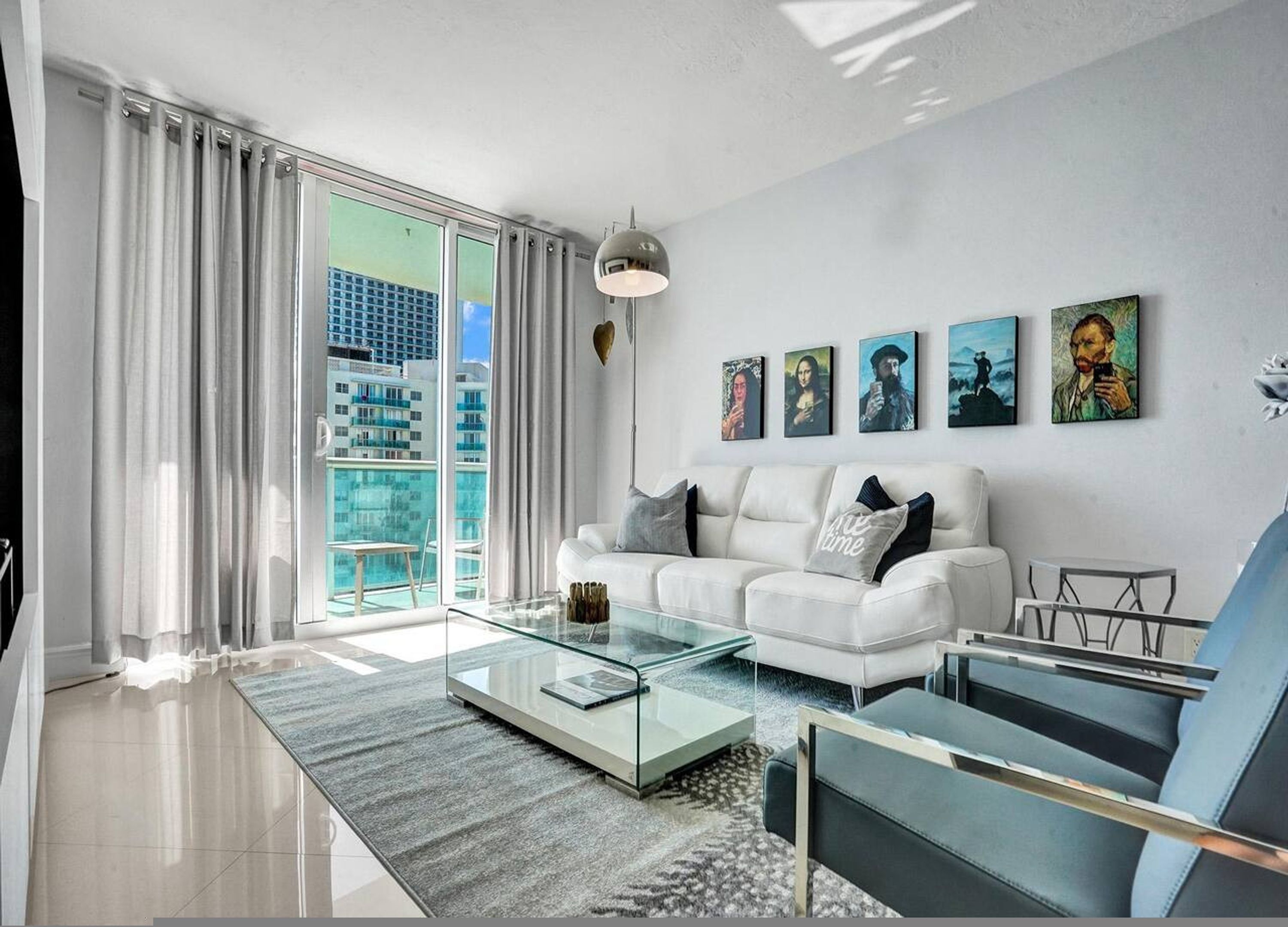 Un salon moderne avec un canapé blanc, une table basse en verre et des œuvres d’art accrochées au mur.