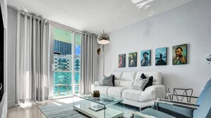 Una sala de estar moderna con un sofá blanco, una mesa de centro de vidrio y una obra de arte en la pared.