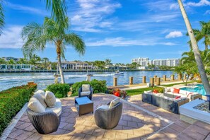 A waterfront patio with wicker furniture, a pool, and a view of the river and buildings. - Serenity Villa Water Front (Lauderdale-by-the-Sea)