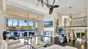 A spacious living room with a large window overlooking a pool, a staircase with a railing, and a ceiling fan.