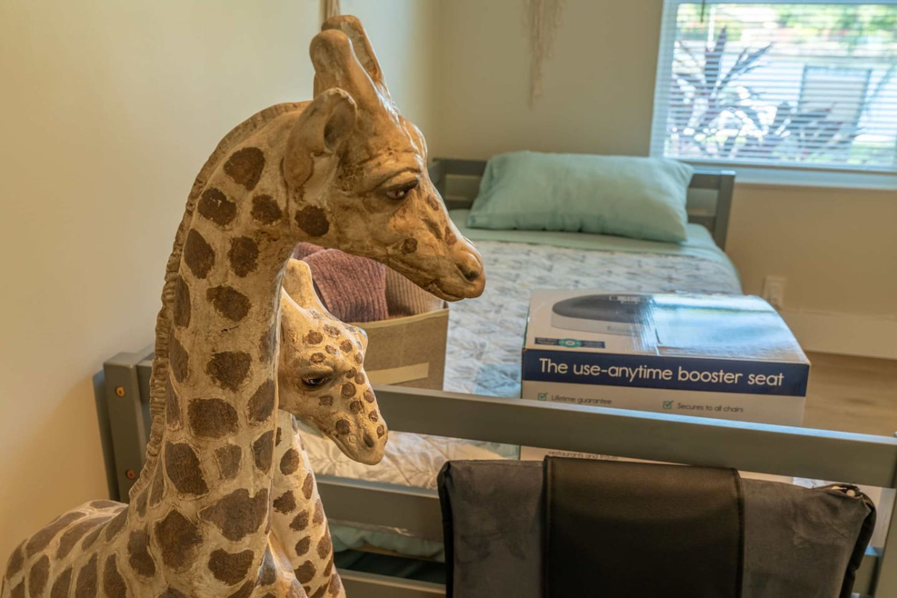 A giraffe statue in a room with a bed and a box labeled "The use-anytime booster seat."