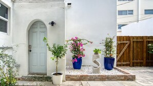 Un edificio blanco con puerta gris, plantas en macetas y una valla de madera.