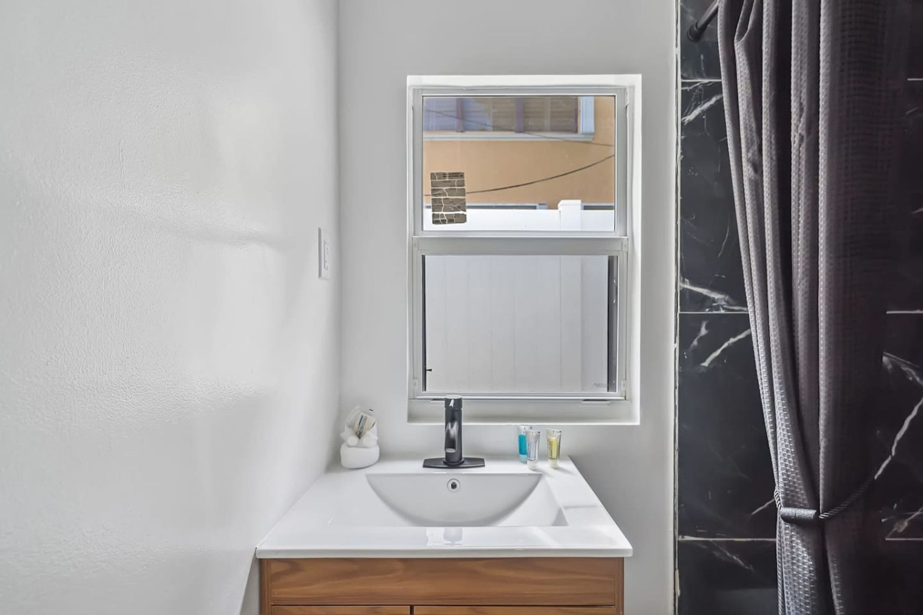 A bathroom with a white sink, a mirror above it, and a window with a view of the outside.