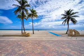 Una playa con palmeras, un sendero pavimentado y cielo despejado.