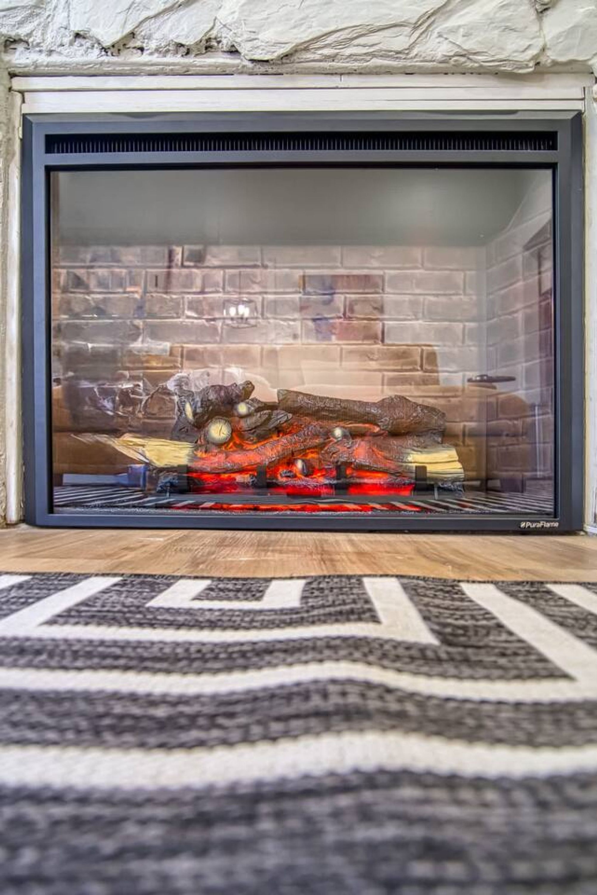 A fireplace with a glass door, a brick wall behind it, and a rug in front.